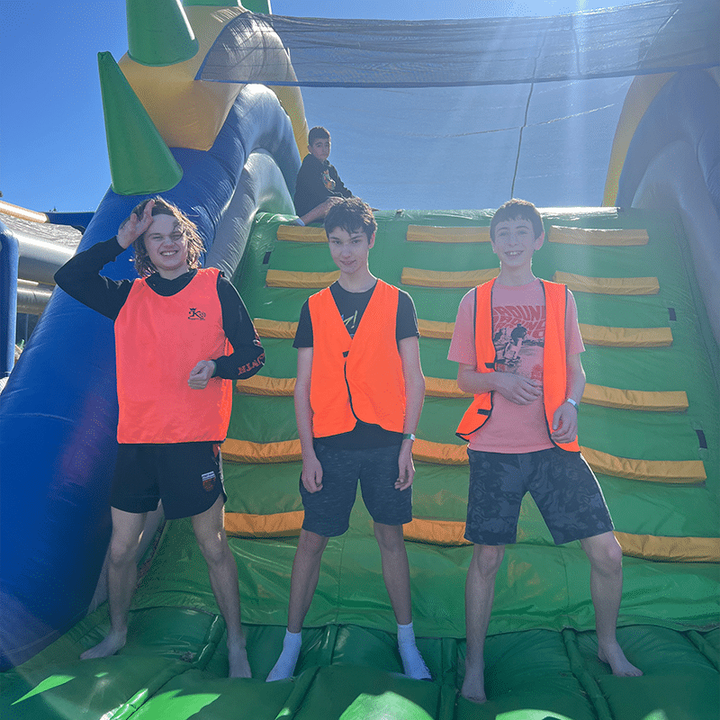 Three boys standing together and the bottom of an inflatable slide